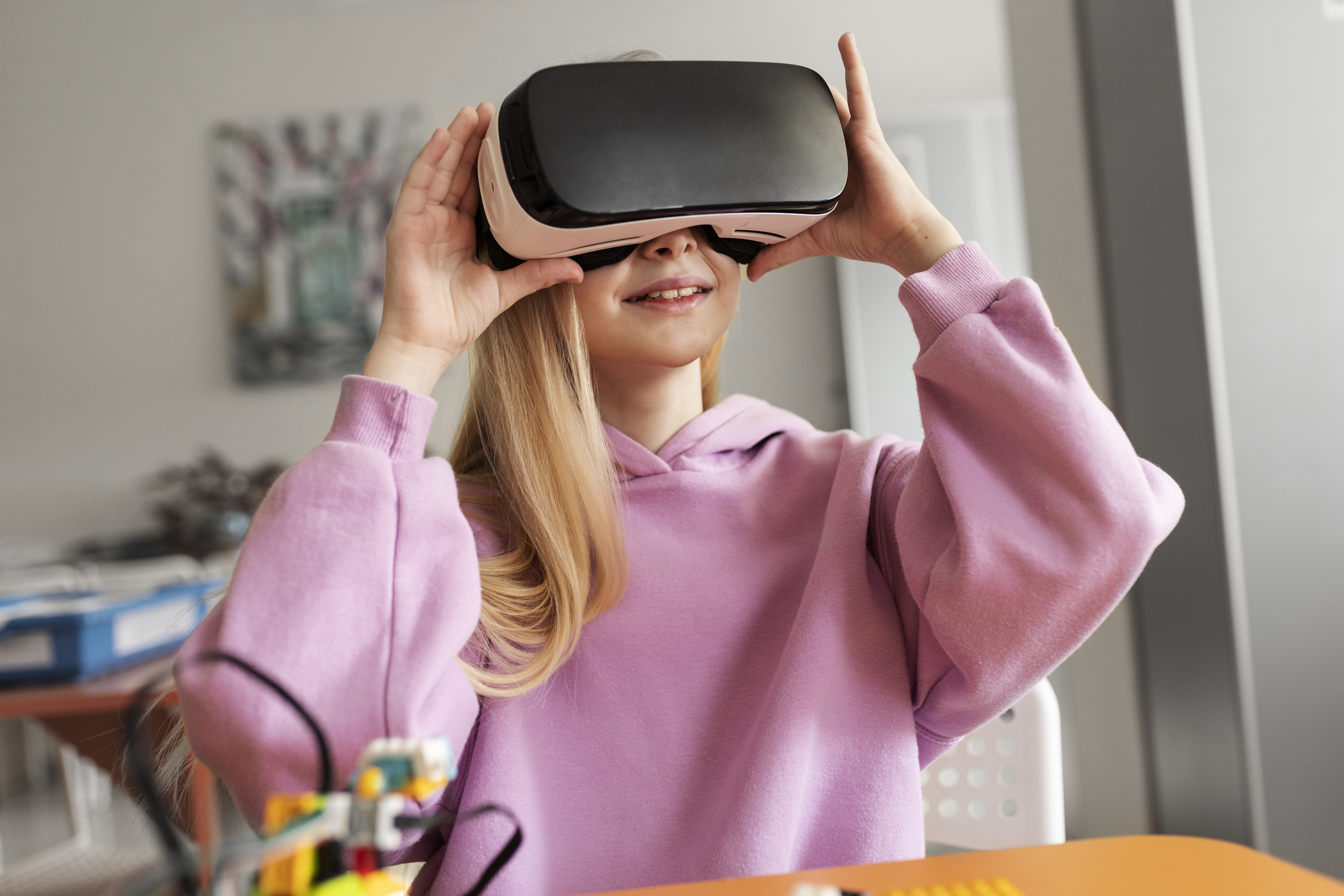 A girl in a pink sweater holds up a K square edutainment VR headset, immersing herself in a virtual reality experience.