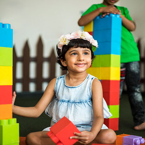 A young girl sits in front of a vibrant stack of blocks, showcasing her creativity and imagination.