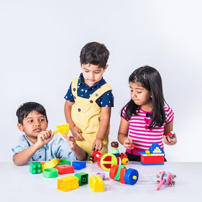 Three children happily play with K square edutainment toys on a white table, engaging in imaginative and creative play.